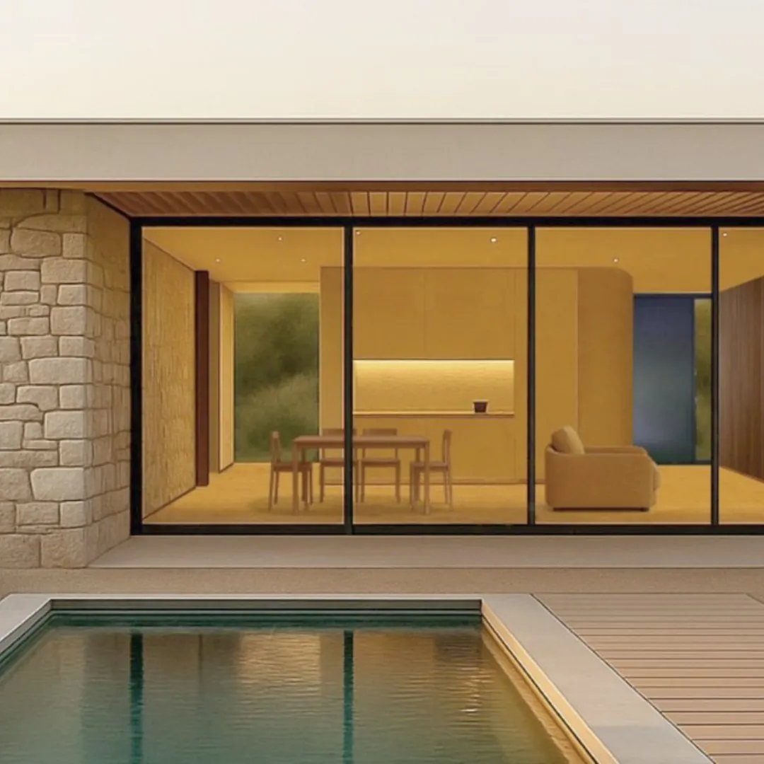 Casa modular MODU Marina al anochecer: ventanales de suelo a techo abiertos al salón y la cocina iluminados, muro de piedra y piscina en primer término.