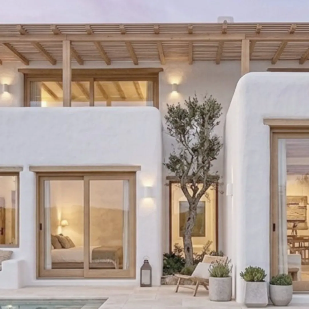 Casa modular MODU Menorca: volúmenes encalados con pérgola de madera, un olivo y una piscina, con el dormitorio abierto al patio.
